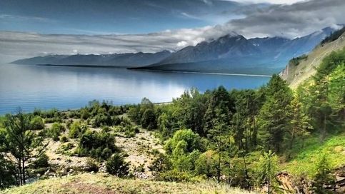 Вид на озеро Байкал, в горах идет сильный дождь, а на берегу солнце